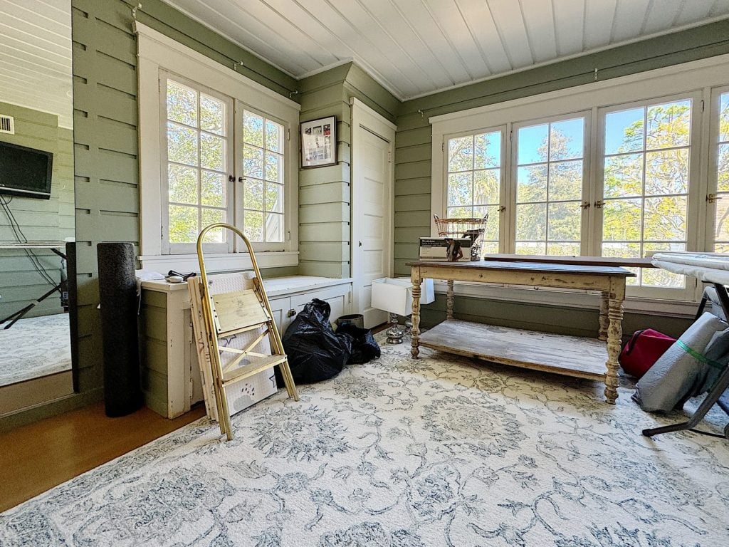 A bright, spacious room with large windows, furnished with a wooden table, built-in bench bench, and a patterned rug.