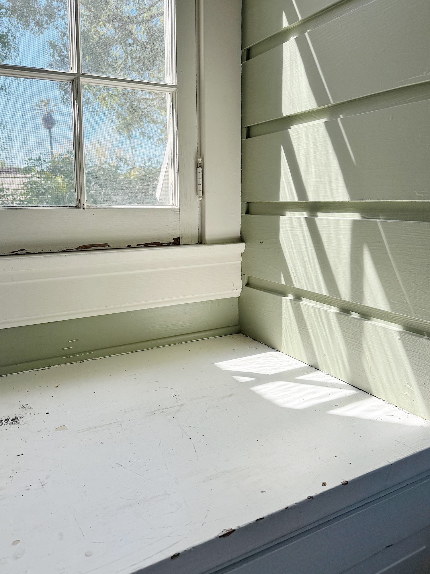 A bright, spacious room with large windows, furnished with a wooden table, built-in bench bench, and a patterned rug.