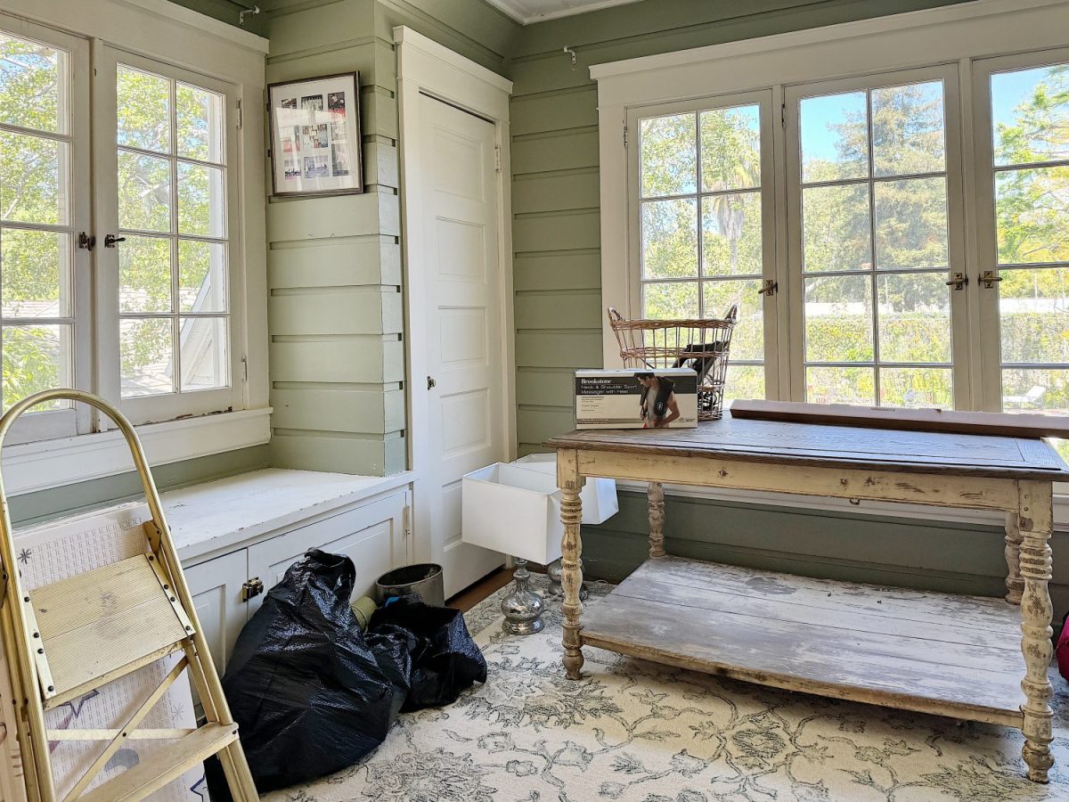 A bright, spacious room with large windows, furnished with a wooden table, built-in bench bench, and a patterned rug.