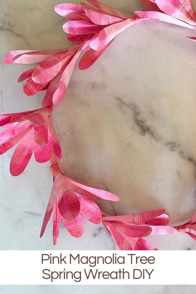A handmade pink magnolia tree spring wreath displayed on a marble background.