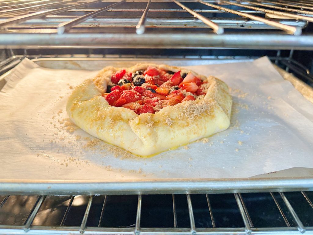 A fruit galette baking in an oven on a lined baking tray.