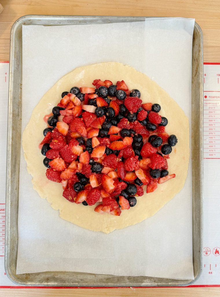 Unbaked galette dough on a baking sheet topped with fresh strawberries, raspberries, and blueberries.