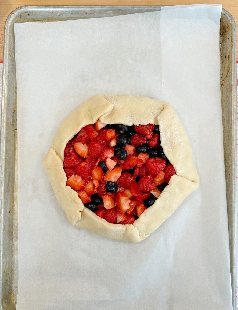 Unbaked galette filled with fresh raspberries, strawberries and blueberries on a parchment-lined baking tray.