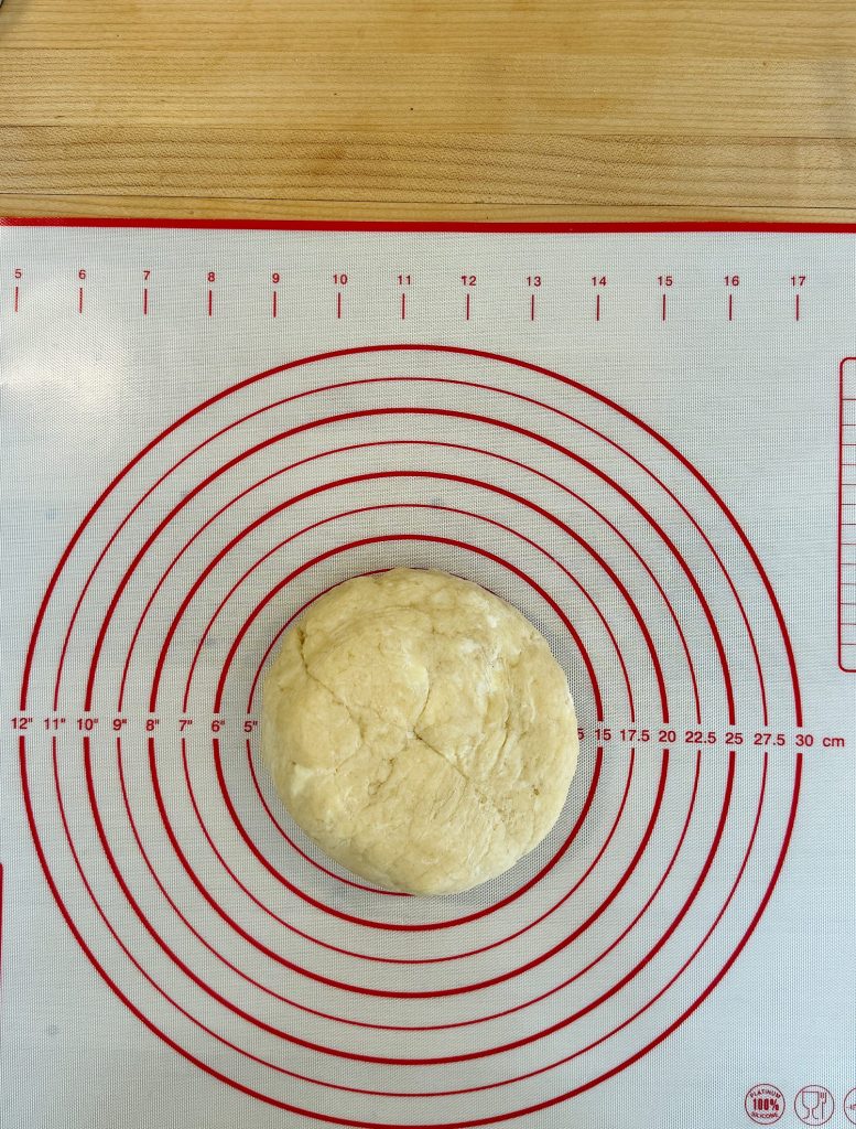 A ball of dough placed on a circular measurement mat marked with concentric red circles and a ruler for size reference.