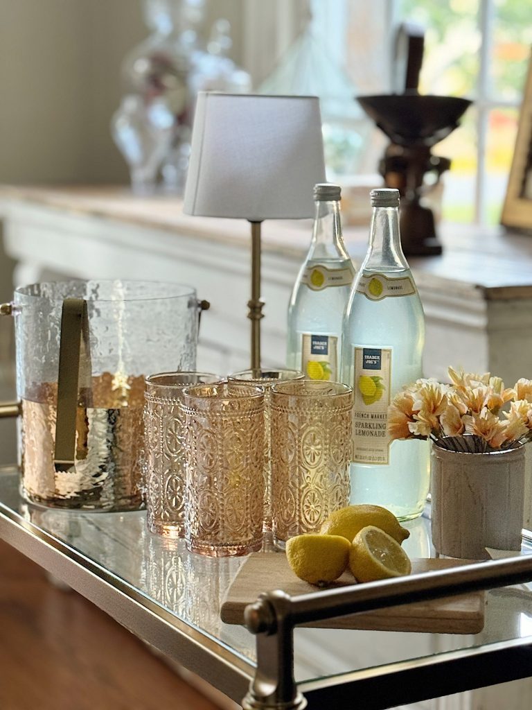 A home setup on a bar cart displaying a vase of paper flowers, non-alcoholic drink items, and sparkling lemonade.