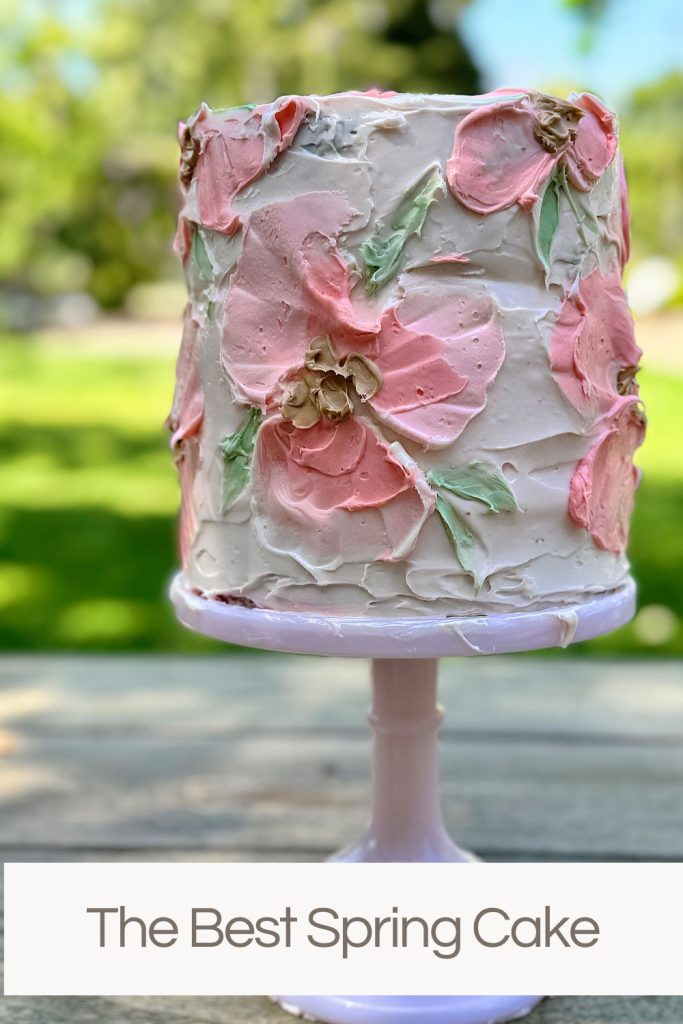 A tall, layered spring cake adorned with pink and green floral frosting, displayed outdoors with a caption "the best spring cake" below it.