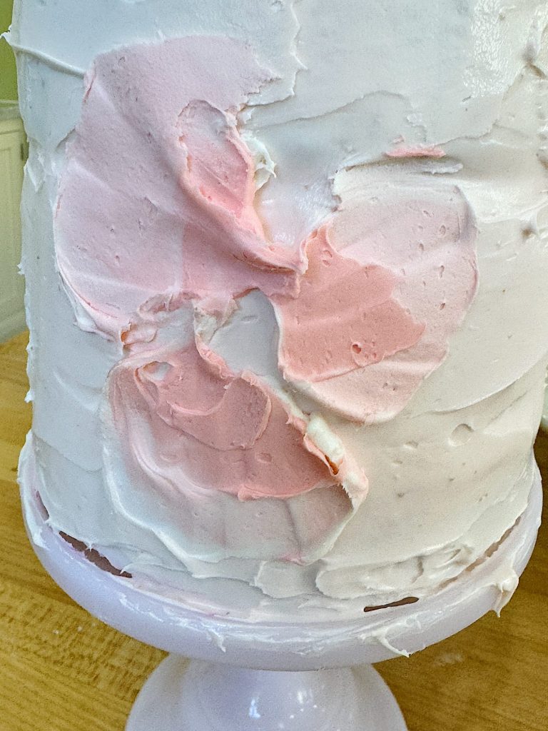 A close-up of a cake with large smudges of pink icing on a white frosting background, displayed on a cake stand.