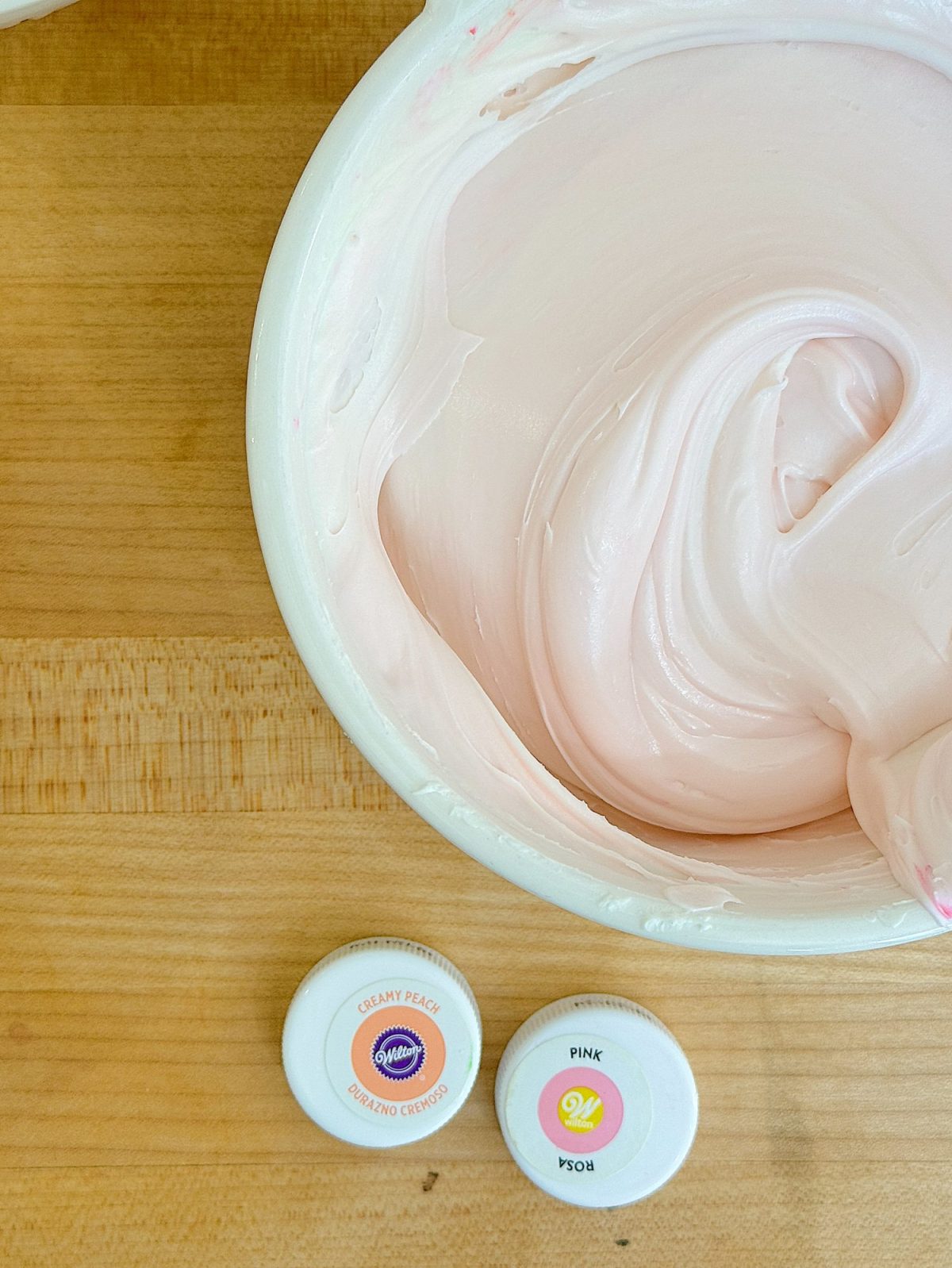 Top view of frosting a cake with creamy pink white icing, with pink and orange gel coloring.