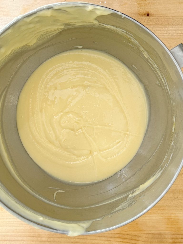 A stainless steel bowl containing creamy cake batter on a wooden surface.