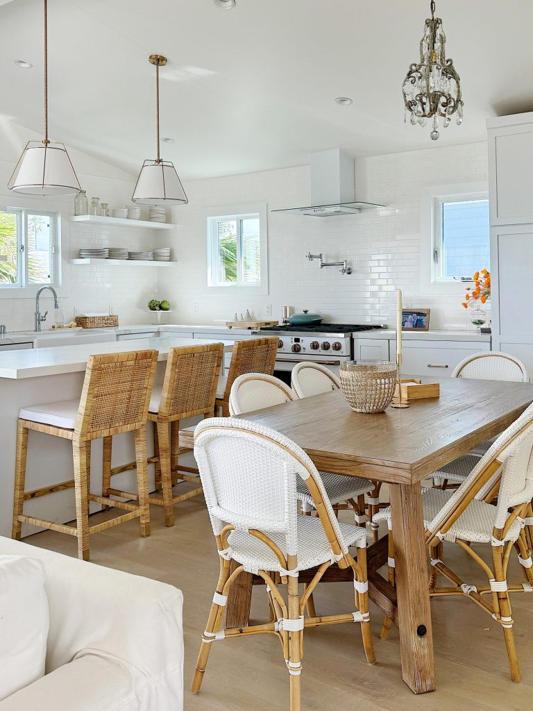 Bright, modern kitchen with white cabinetry, a wooden dining table, bar stools, and pendant lighting, showcasing a clean, airy design.