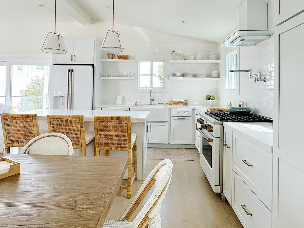 Bright, modern kitchen with white cabinetry, subway tiles, a wooden dining table, wicker chairs, and pendant lights.