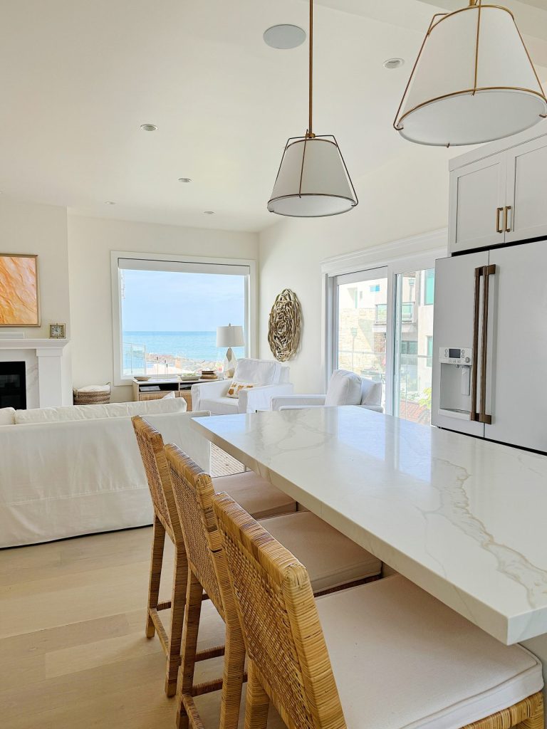 Bright, open-plan kitchen and dining area with modern beach decor, large windows with ocean view, and pendant lighting.
