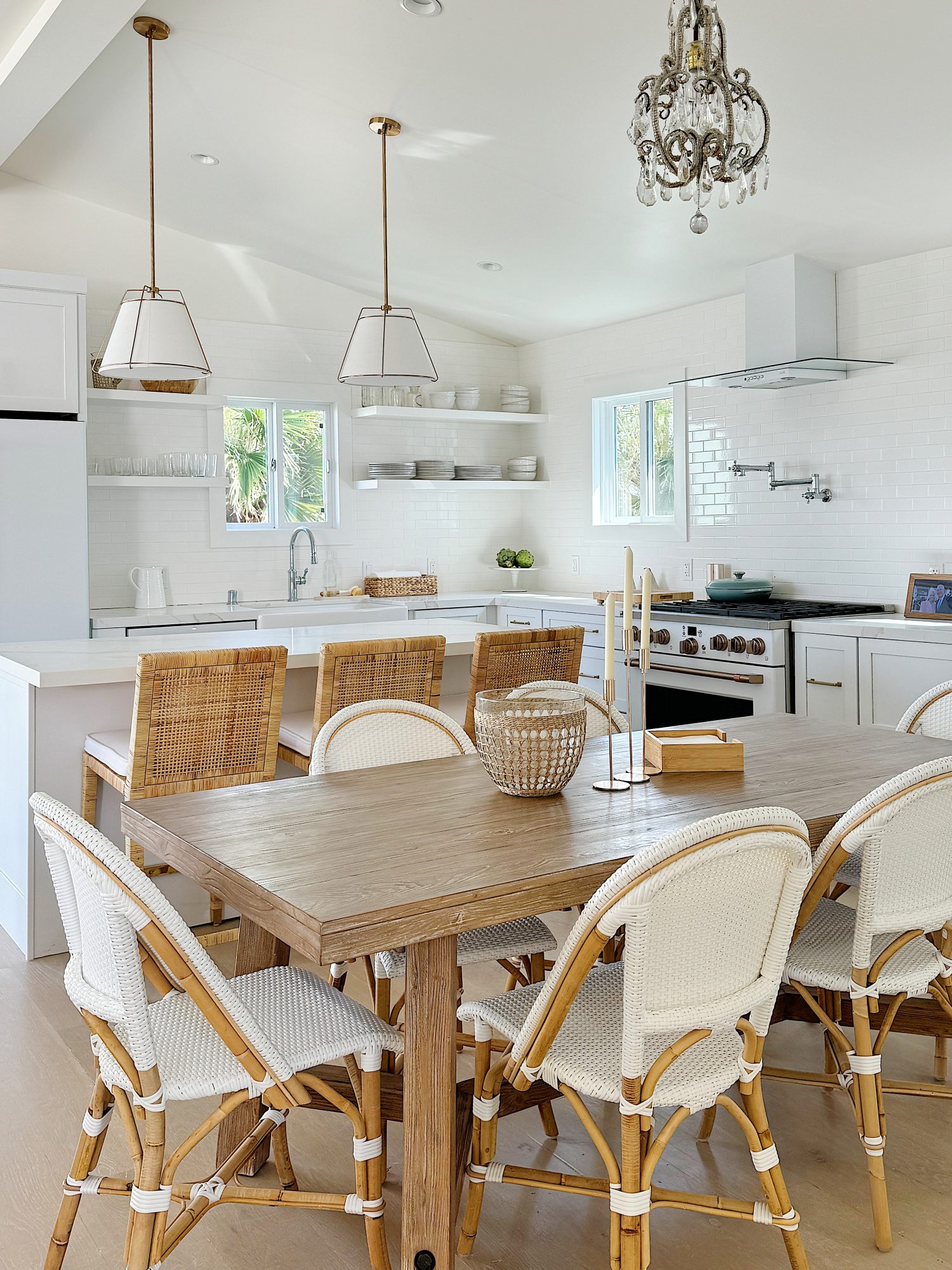Bright, modern kitchen with wooden dining table, wicker chairs, white cabinets, and hanging pendant lights.