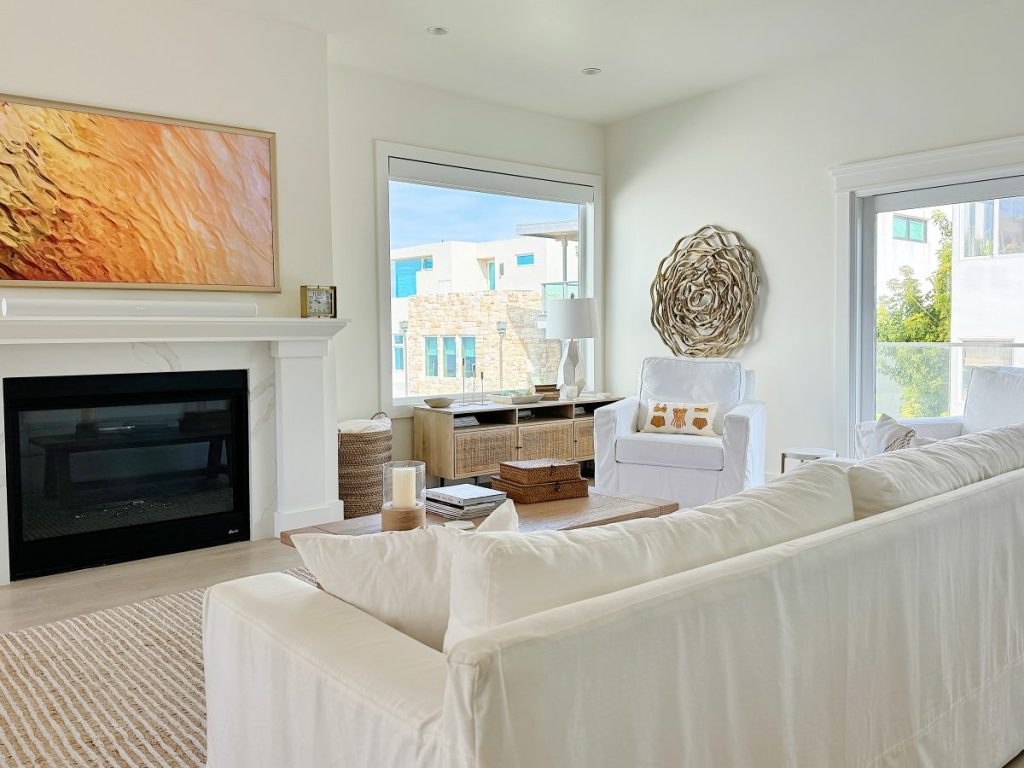 Bright, modern living room with a white sofa facing a fireplace, large screen tv, and a view through a glass door. decor includes a spiral wall art and an abstract painting.