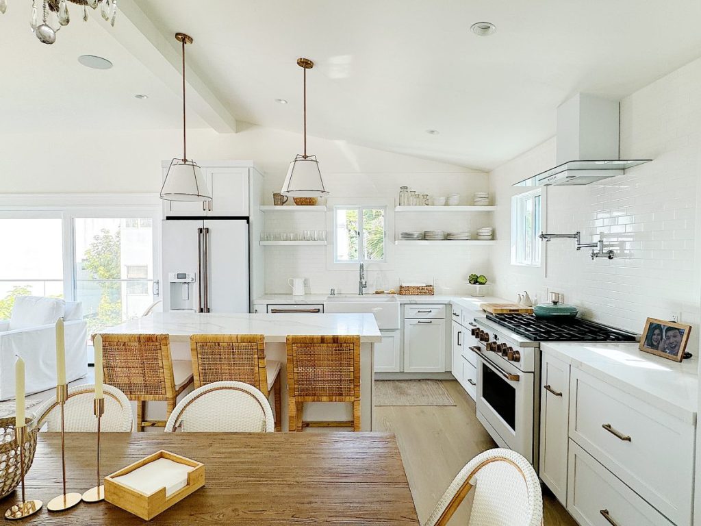 Bright, modern kitchen with white cabinets, subway tile backsplash, stainless steel appliances, and a dining area with wicker chairs.