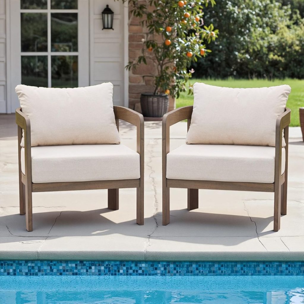 Two cushioned wooden chairs with beige upholstery sit side by side on a patio next to a swimming pool, creating inviting outdoor porch decor amid lush greenery and a house in the background.