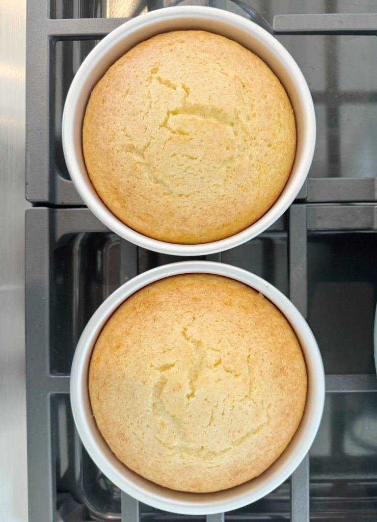 Two round cakes in white ramekins, baked to a light golden brown, placed on a stove.