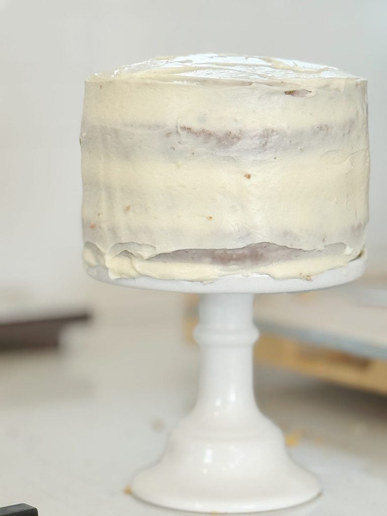 A homemade cake with white frosting on a white cake stand.