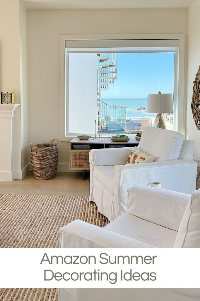 Bright living room with white armchairs, a striped rug, basket, and a window showing a balcony with a spiral staircase and ocean view. Text reads: "Amazon Summer Decorating Ideas.