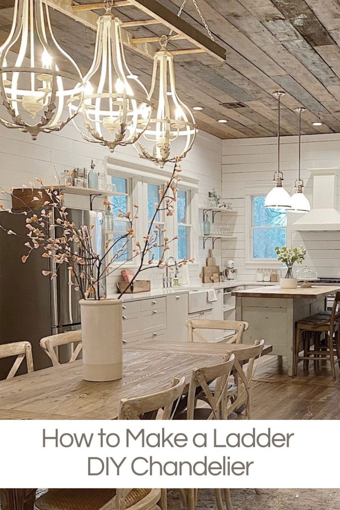 Kitchen with wooden ceiling, rustic white cabinets, and a wooden dining table. Three large, ladder-style chandeliers are hanging from the ceiling. Text at bottom reads "How to Make a Ladder DIY Chandelier.