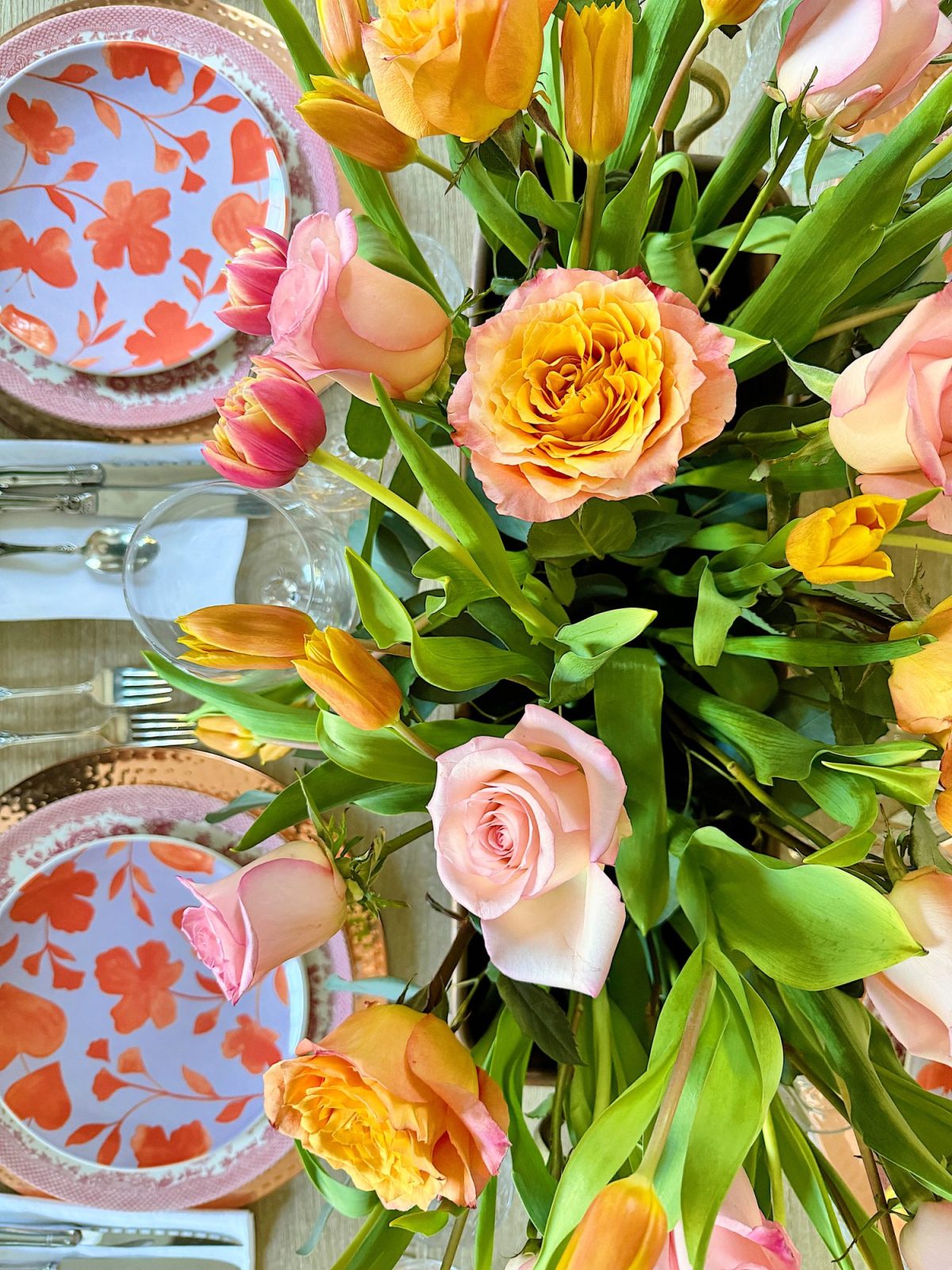 Elegant dining table setting with a floral centerpiece, colorful plates, and crystal glassware, in a room with natural light.
