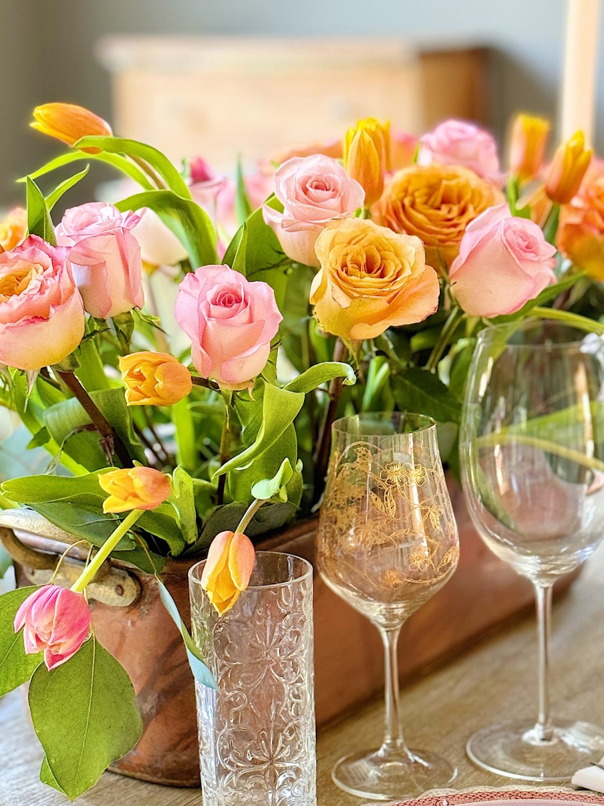 Elegant dining table setting with a floral centerpiece, colorful plates, and crystal glassware, in a room with natural light.