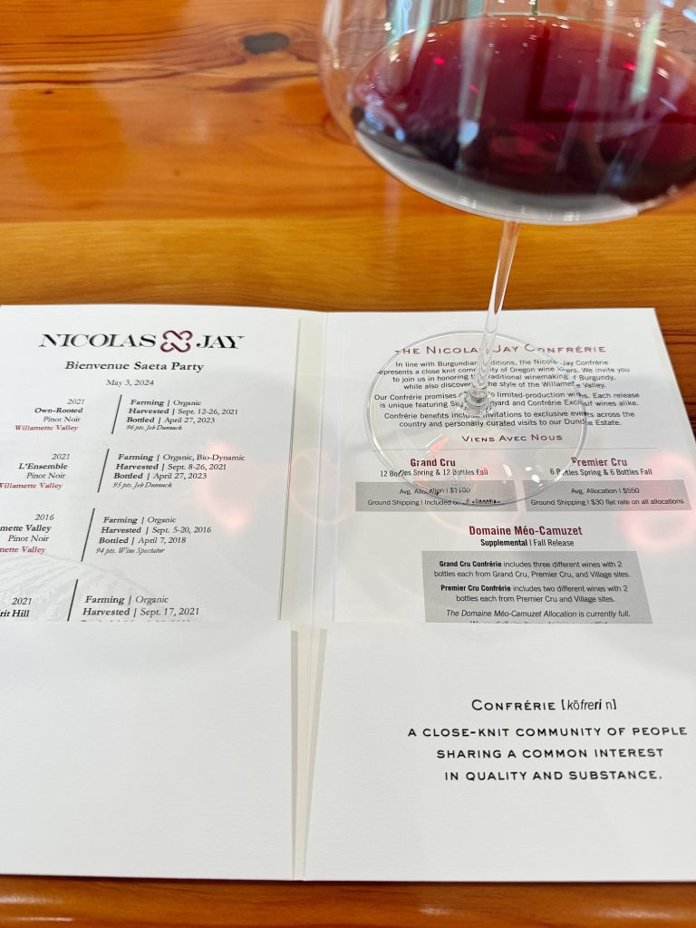 Glass of red wine next to a wine tasting menu on a wooden table.
