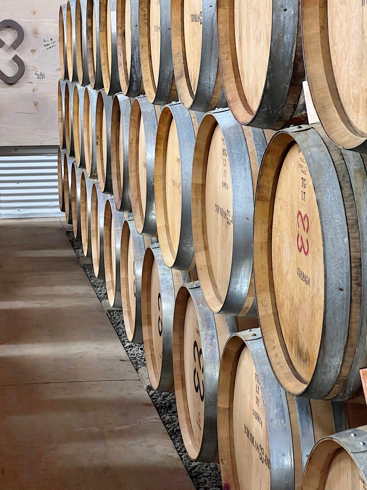Rows of wooden barrels stacked in a cellar, some labeled with numbers, in a dimly lit storage area.