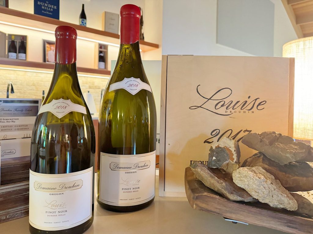 Two bottles of domaine drouhin pinot noir displayed with geological samples and a ‘louise drouhin 2014’ booklet on a table.