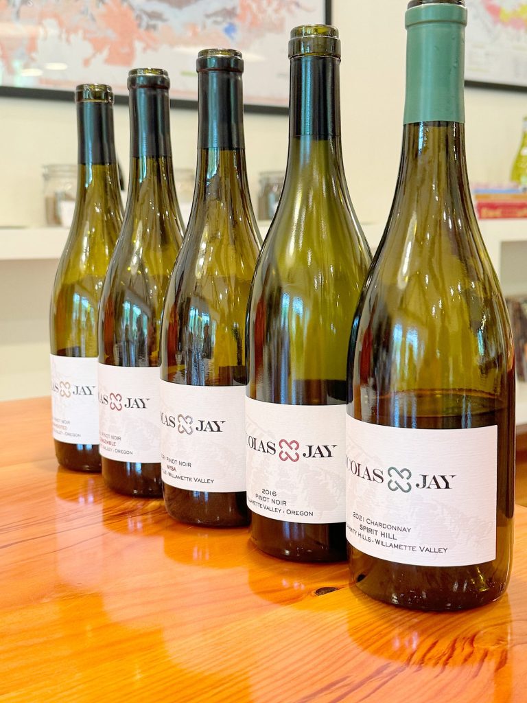 Five bottles of Nicholas Jay vineyards wine in a row on a table, with focus on the labels, against a blurred café backdrop.
