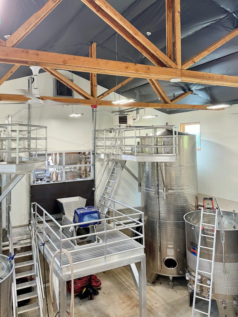 Interior of a brewery with stainless steel tanks, industrial equipment, and wooden beams supporting the ceiling.