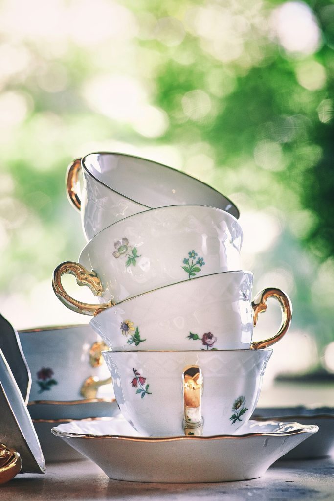 A stack of elegant floral-patterned teacups with gold handles, positioned against a soft-focus green background.