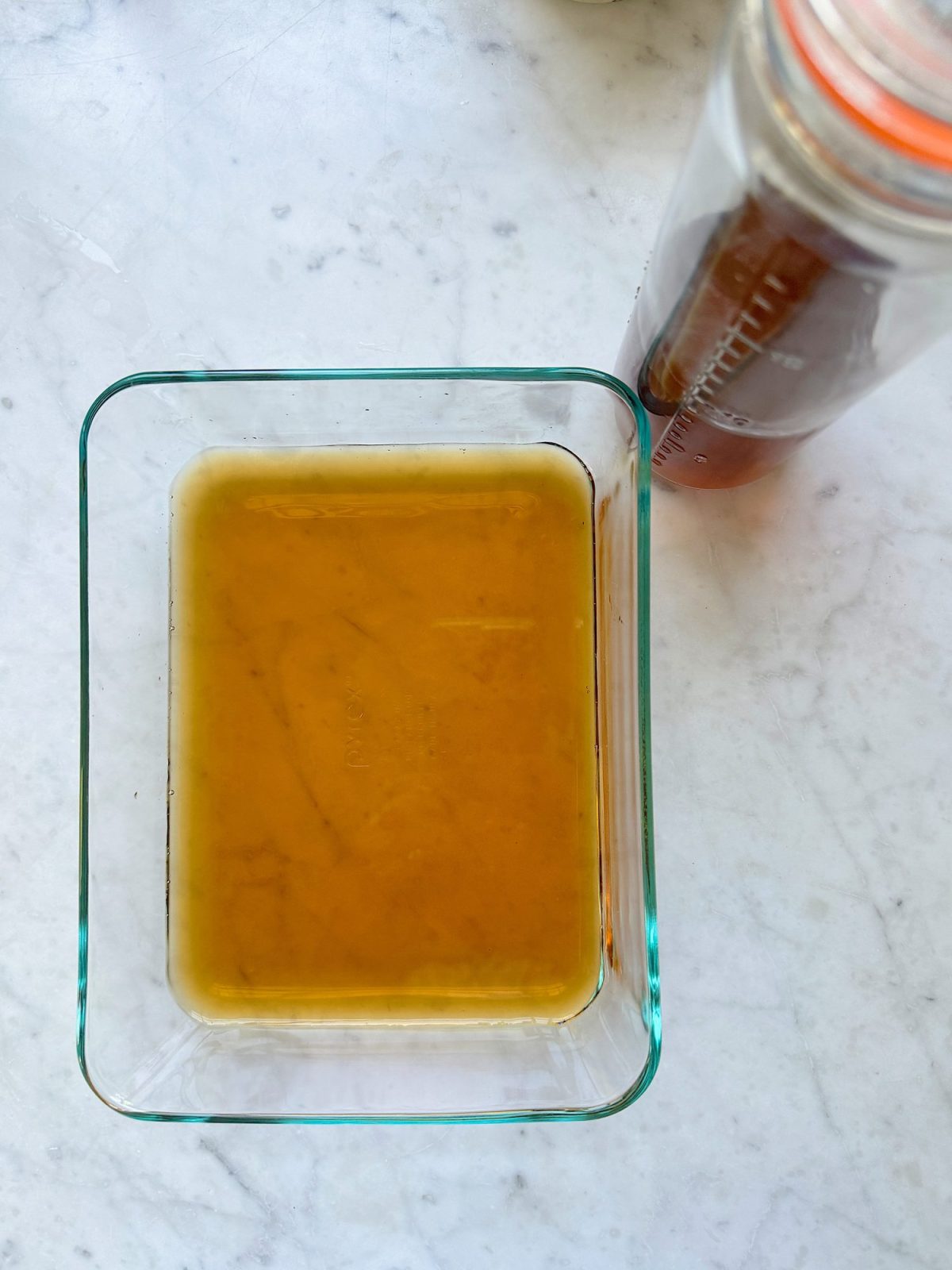 A glass container holding homebrewed tea, with a jar of additional tea nearby on a marble surface.