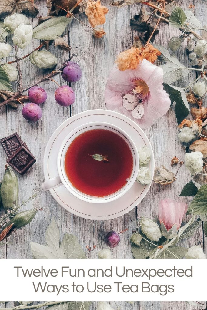A cup of tea with a mint leaf, surrounded by flowers and a piece of chocolate, on a wooden surface.