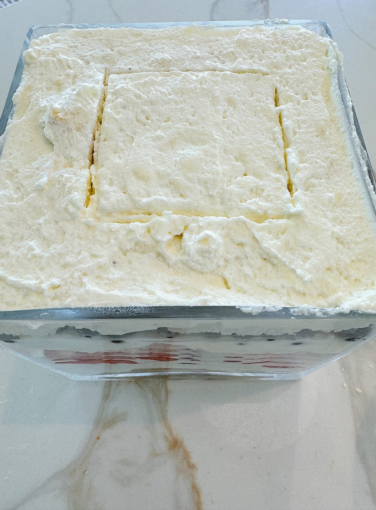 A square glass dish filled with fluffy, white whipped cream with a smaller square area that appears to have been partially removed.