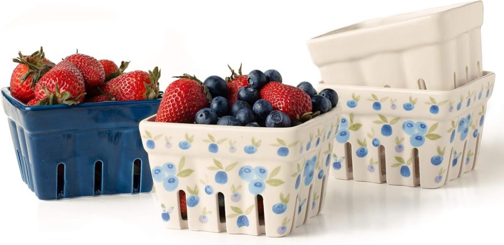 Three ceramic berry baskets—one blue, one cream-colored with a blueberry pattern, and one plain cream—hold a vibrant mixed berry assortment of strawberries and blueberries.