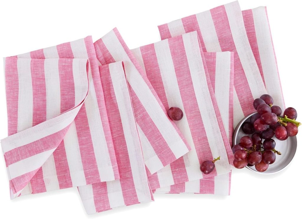 Five pink and white striped cloth napkins are arranged on a flat surface with a small bowl of mixed berry grapes and a single loose grape nearby.
