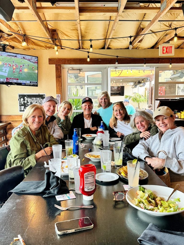 A group of eight people sitting around a table enjoying food and drinks at a casual indoor restaurant.