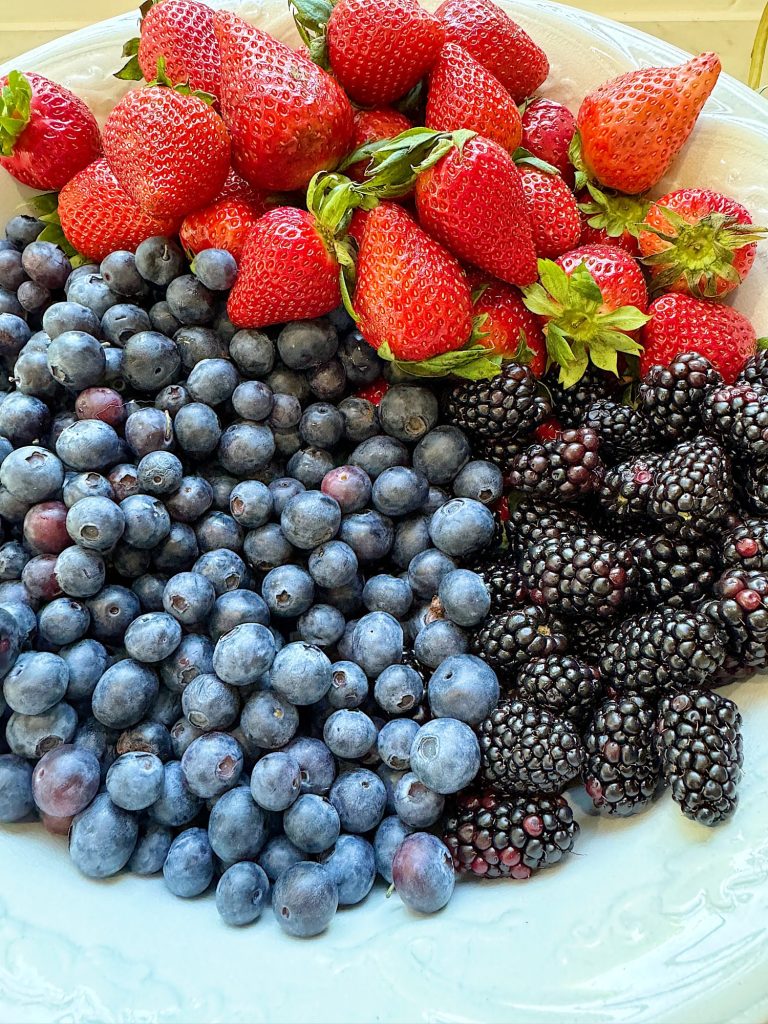 A plate filled with fresh strawberries, blueberries, and blackberries.