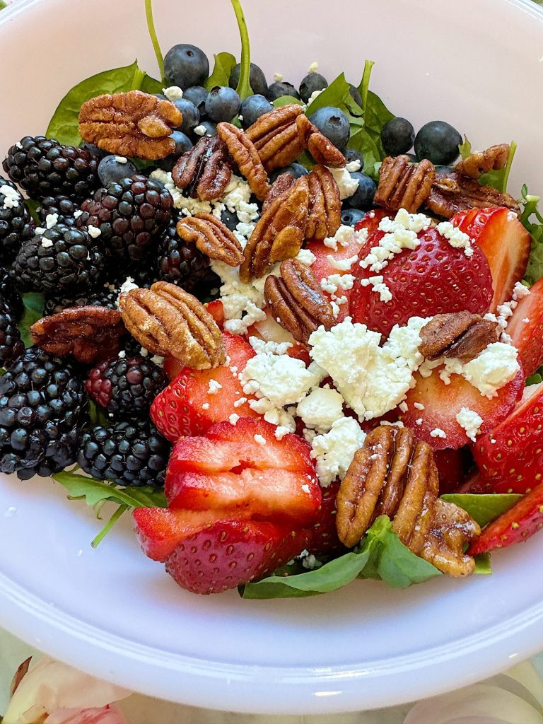 A salad bowl with spinach, sliced strawberries, blackberries, blueberries, pecans, and crumbled feta cheese.