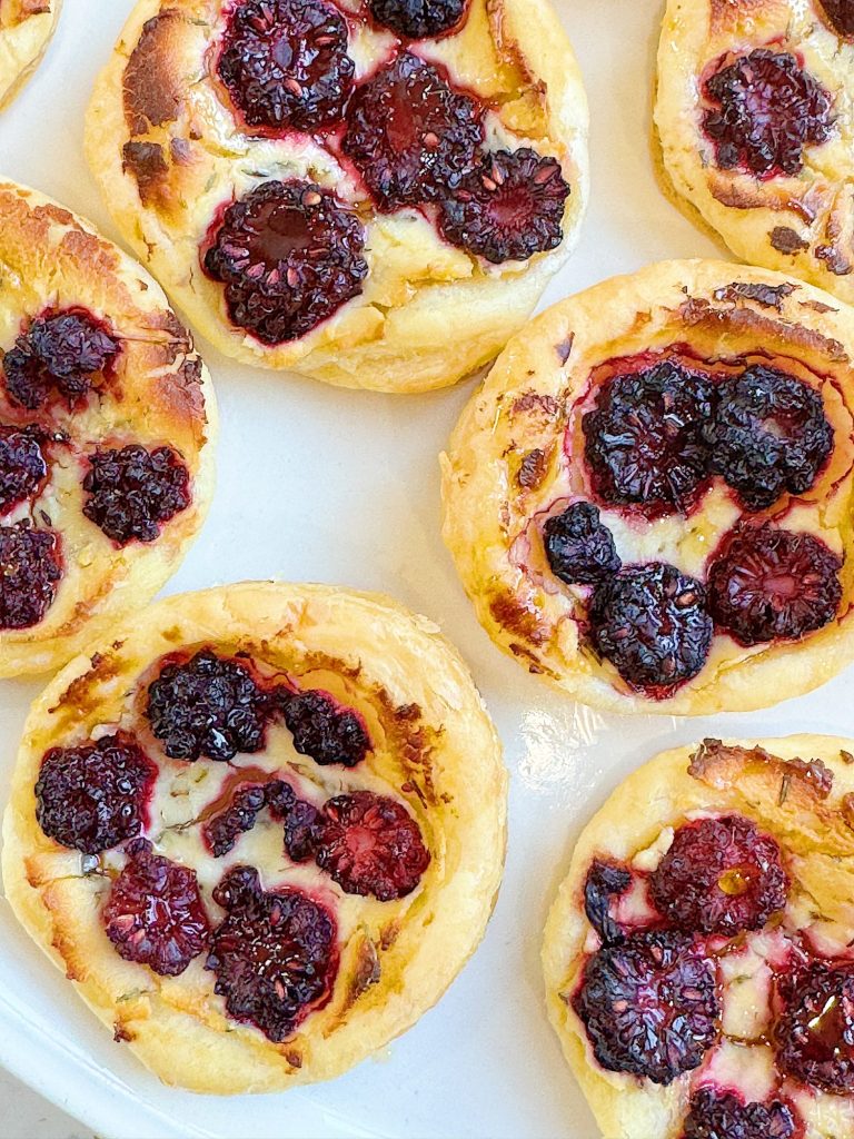 A close-up of freshly baked pastries topped with blackberries on a white surface.