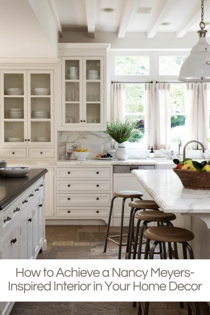 A kitchen with white cabinets, a marble countertop, bar stools, a bowl of apples, and a potted plant near the window. Text overlay reads: "How to Achieve a Nancy Meyers-Inspired Interior in Your Home Decor.