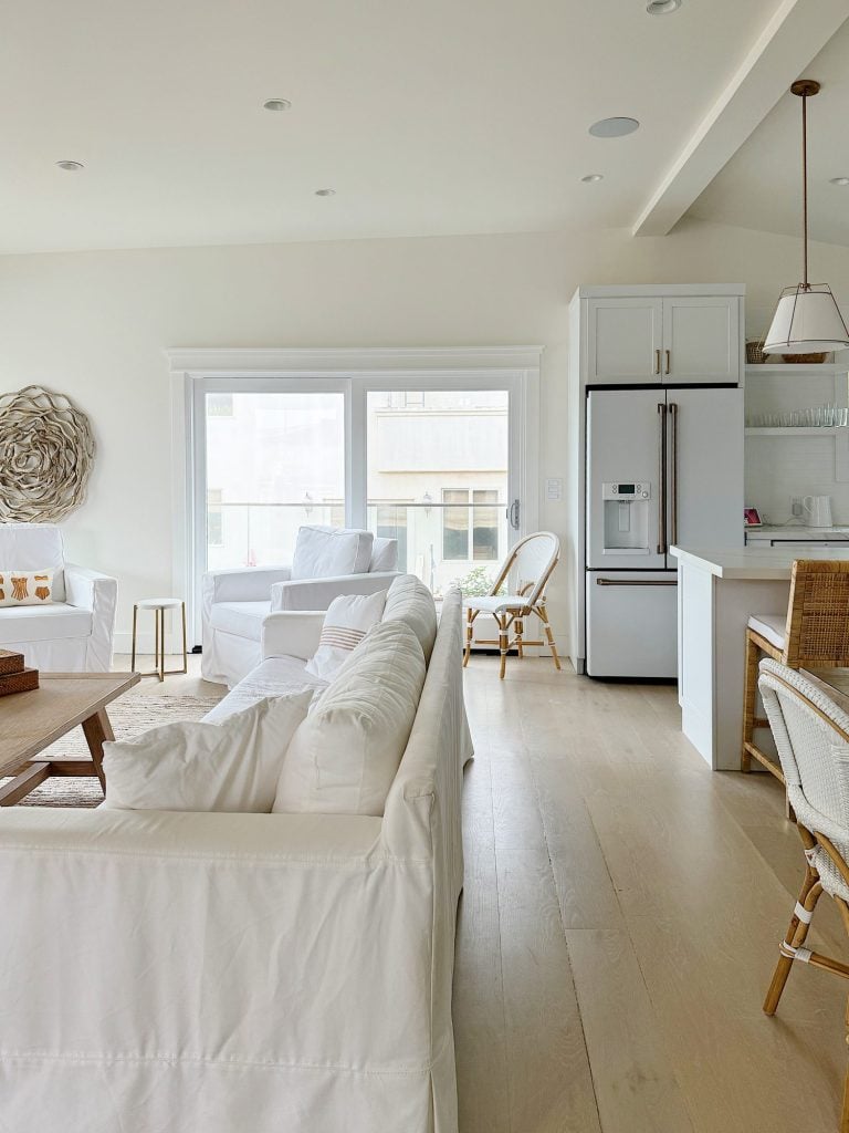 A bright, airy living space featuring white furniture, a modern kitchen area, and large windows that allow natural light to fill the room.