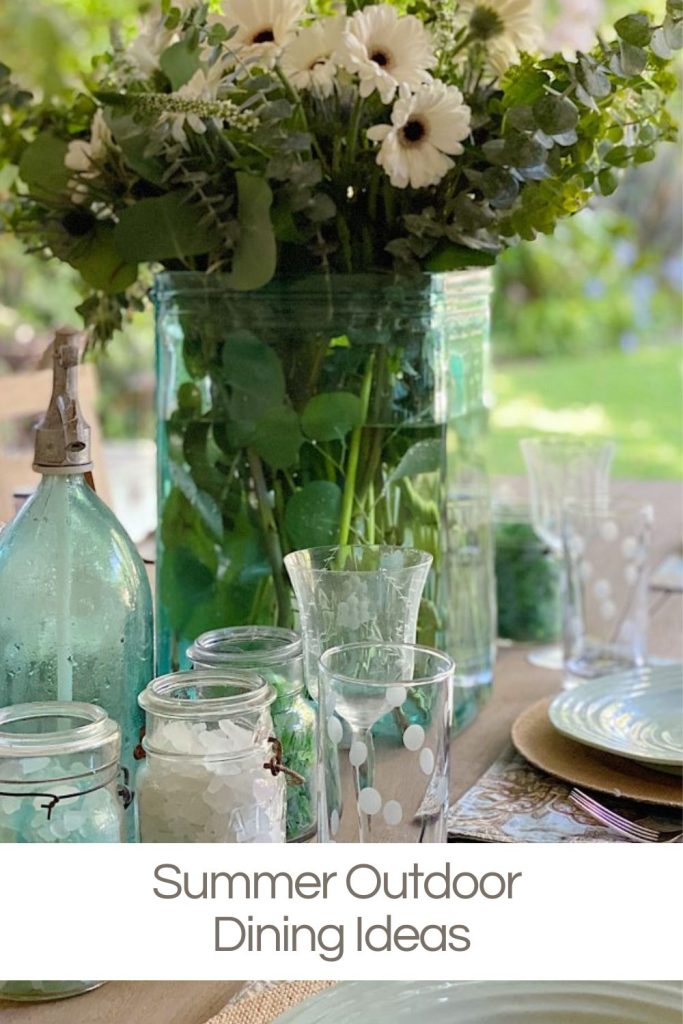 A table set for outdoor dining with a large floral arrangement, glass jars, and glasses. Text overlay reads "Summer Outdoor Dining Ideas.
