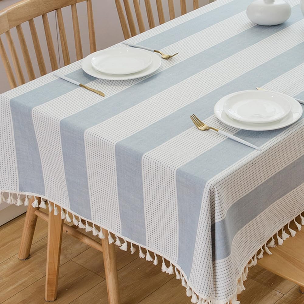 A rectangular table covered with a blue and white striped tablecloth evokes a Summer Beach vibe, set with two plates, two forks, and a vase, surrounded by wooden chairs.