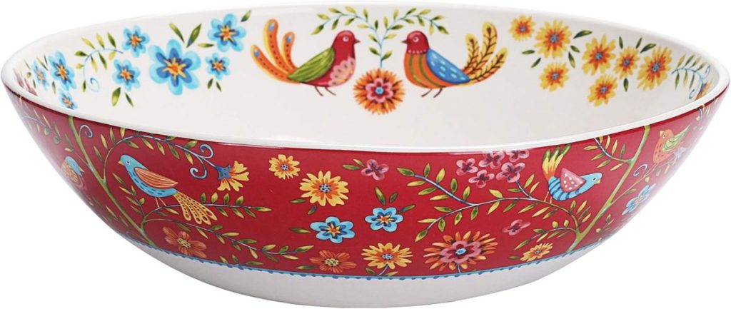 A round ceramic bowl with a red exterior and white interior, decorated with colorful flowers and birds in a folk-art style—perfect for serving your favorite summer chicken recipes.