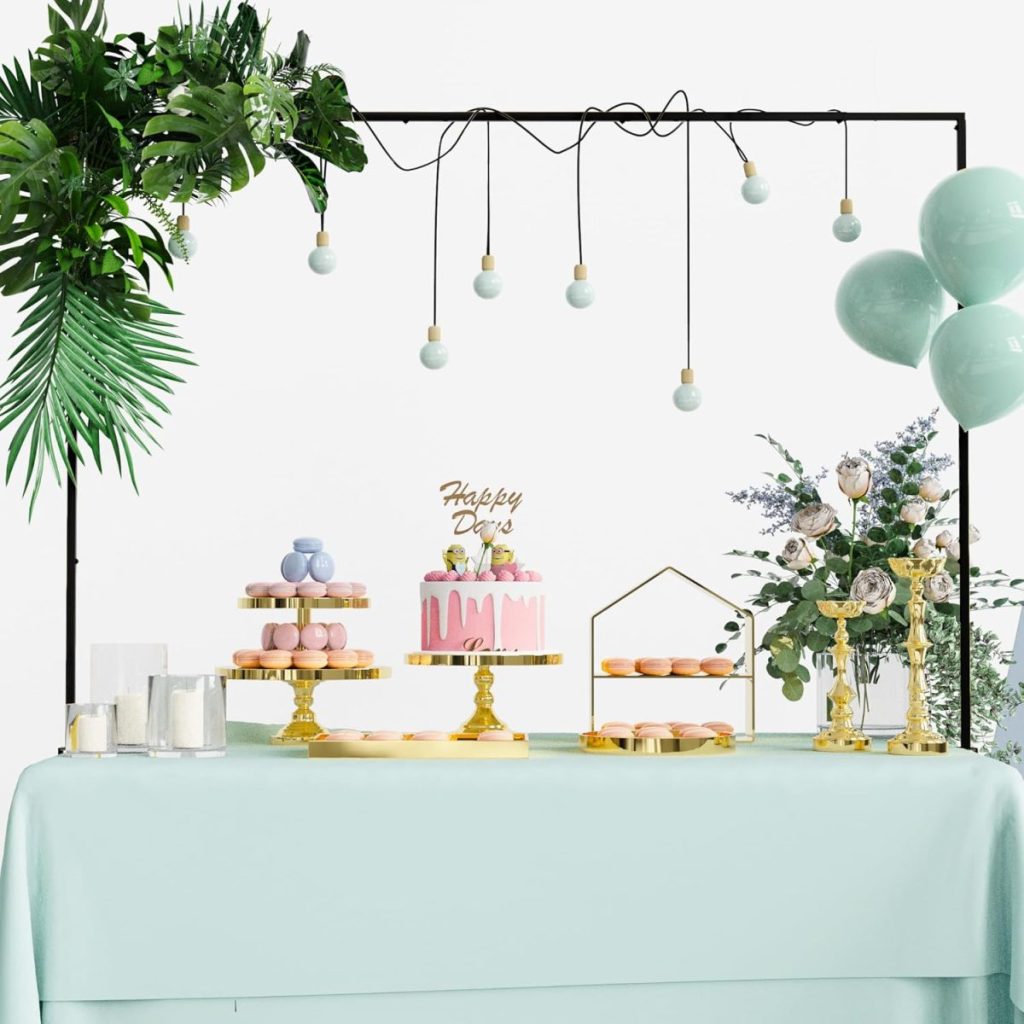 A decorated dessert table with a pink cake, macarons, balloons, hanging light bulbs, greenery, and floral arrangements evokes a Summer Beach vibe against a crisp white background.