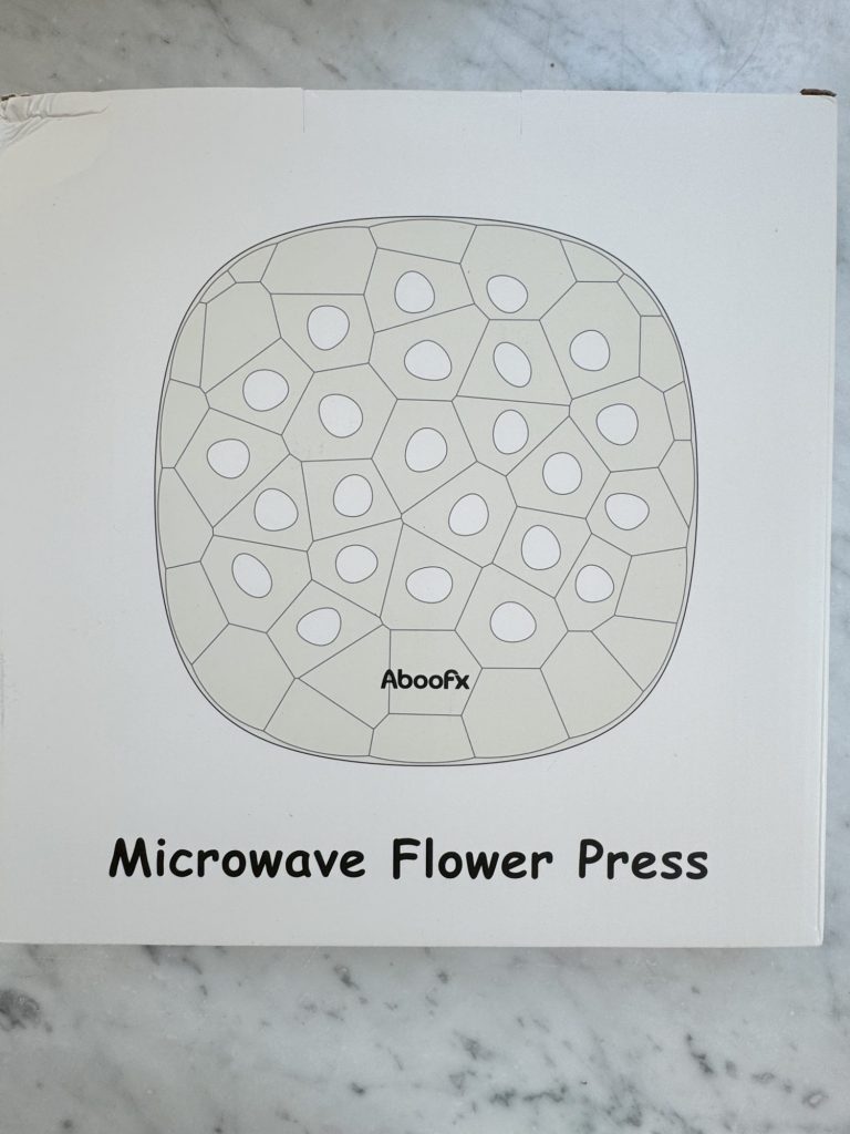 The image shows a box with a design and the text "Aboofx Microwave Flower Press" on it. The design features a geometric pattern with various shapes resembling petals or seeds.