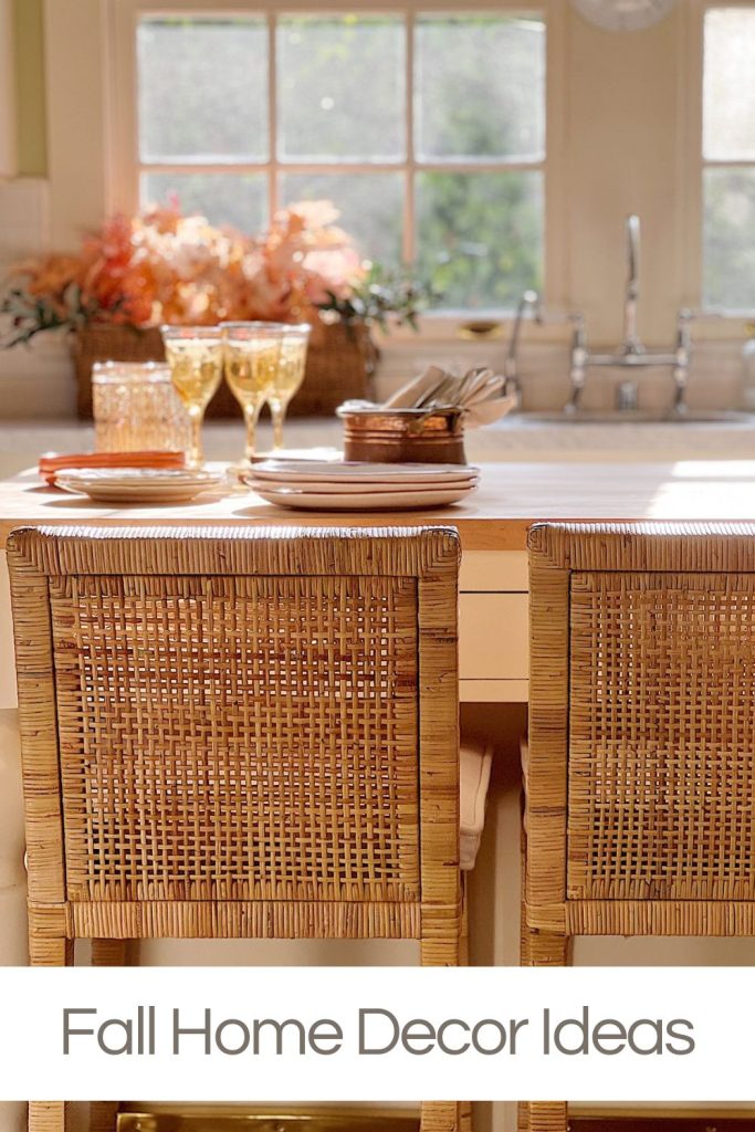 A cozy kitchen island with wicker chairs, autumn-themed flowers, glassware, and fall home decor elements displayed under a soft, natural light. The text reads, "Fall Home Decor Ideas.