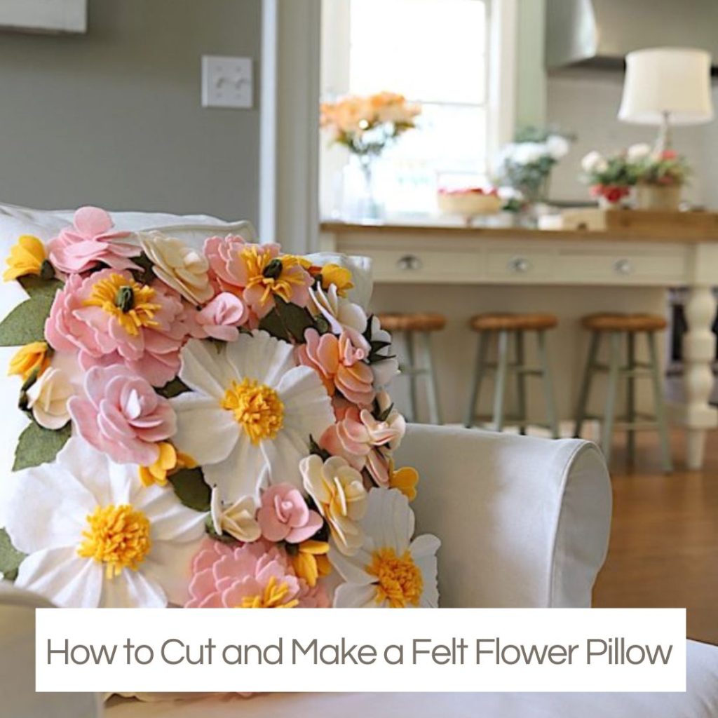 A white armchair with a decorative pillow covered in pink, white, and yellow felt flowers—a charming touch for Creative Crafts lovers; a kitchen with bar stools is seen in the background.